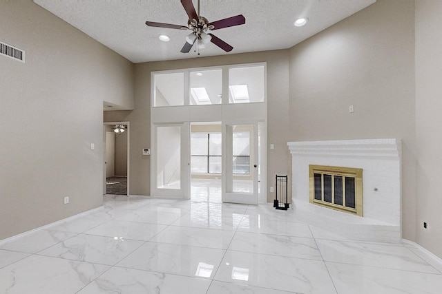 unfurnished living room featuring ceiling fan, a towering ceiling, a textured ceiling, and a fireplace