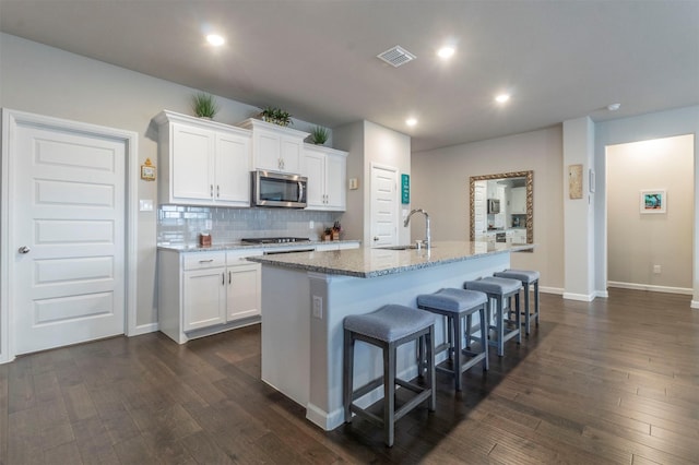 kitchen with a kitchen island with sink, white cabinets, dark hardwood / wood-style floors, and appliances with stainless steel finishes