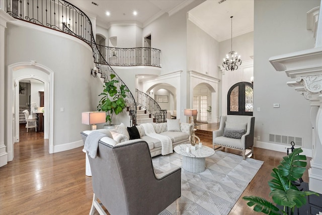 living room with french doors, a towering ceiling, crown molding, hardwood / wood-style flooring, and a notable chandelier