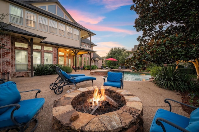 patio terrace at dusk with a fire pit and a pool with hot tub