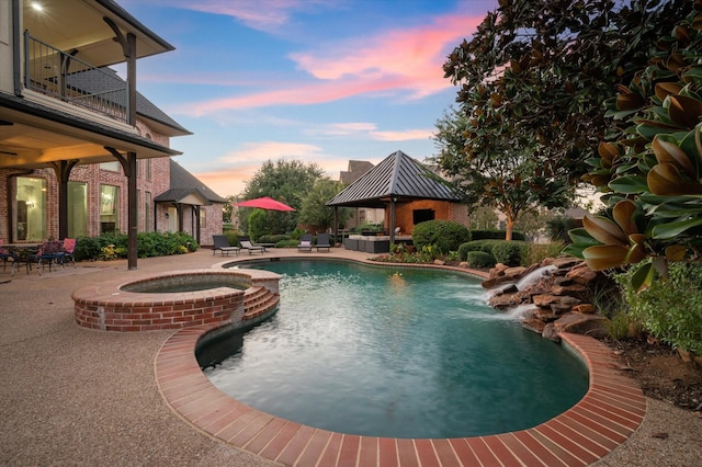 pool at dusk featuring a gazebo, pool water feature, an in ground hot tub, and a patio