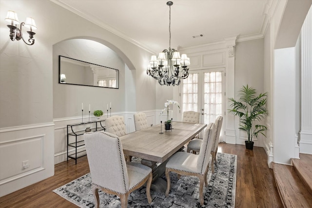 dining area featuring french doors, ornamental molding, dark wood-type flooring, and an inviting chandelier