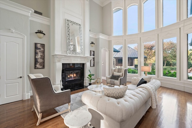 living room featuring a large fireplace, crown molding, dark hardwood / wood-style flooring, and a towering ceiling