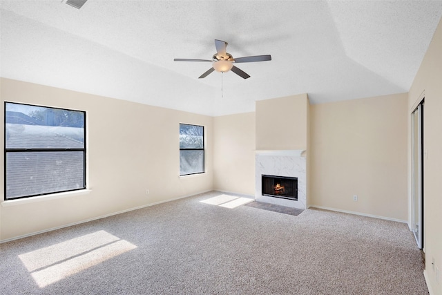 unfurnished living room with light carpet, ceiling fan, a high end fireplace, and a textured ceiling