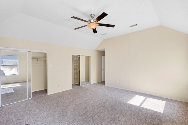 unfurnished bedroom featuring ceiling fan, vaulted ceiling, multiple closets, and carpet flooring