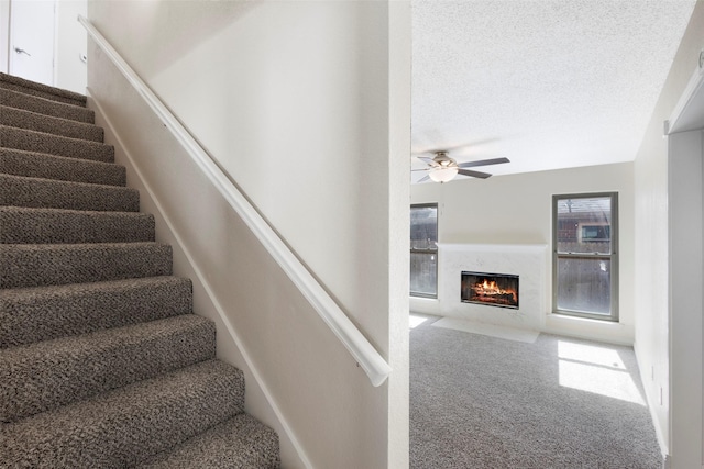 staircase featuring carpet floors, ceiling fan, a high end fireplace, and a textured ceiling