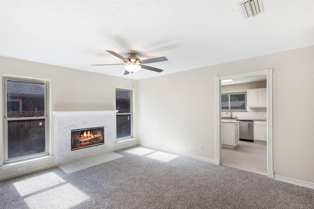 unfurnished living room with ceiling fan, light colored carpet, a textured ceiling, and a fireplace