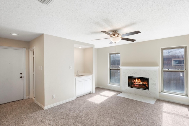 unfurnished living room with ceiling fan, light colored carpet, a high end fireplace, and a textured ceiling