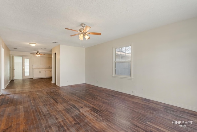 empty room with a textured ceiling, ceiling fan, and dark hardwood / wood-style floors