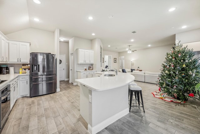 kitchen featuring lofted ceiling, light wood-type flooring, an island with sink, appliances with stainless steel finishes, and white cabinetry