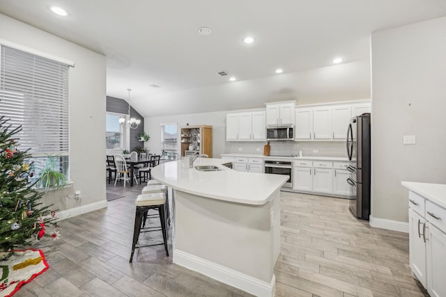 kitchen featuring white cabinetry, sink, lofted ceiling, a kitchen island with sink, and appliances with stainless steel finishes