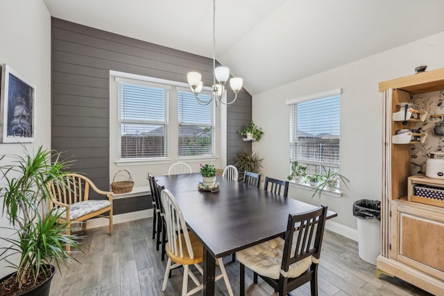 dining space with wooden walls, a chandelier, lofted ceiling, and light wood-type flooring