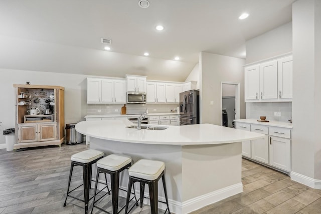 kitchen with sink, white cabinets, stainless steel appliances, and a center island with sink