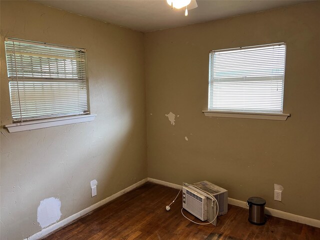 empty room featuring dark hardwood / wood-style flooring, a wall unit AC, and plenty of natural light