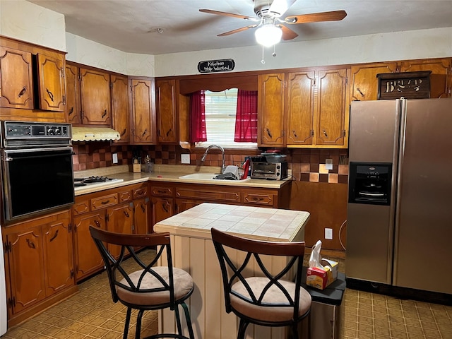 kitchen featuring a breakfast bar, white gas stovetop, sink, stainless steel fridge, and black oven