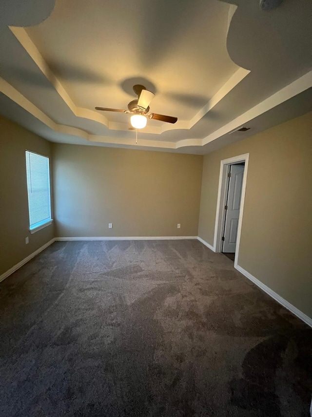 spare room featuring dark colored carpet, a tray ceiling, and ceiling fan