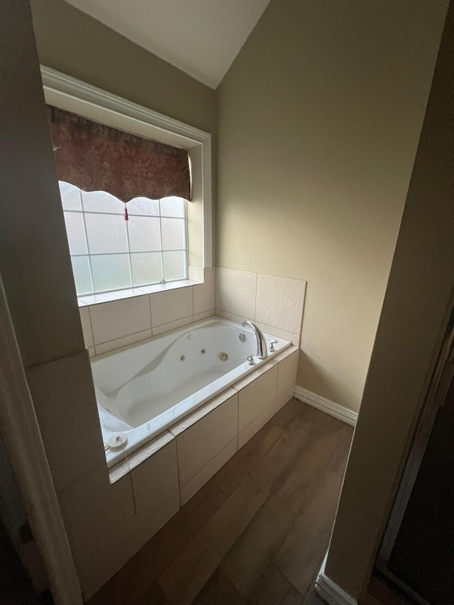 bathroom with wood-type flooring, lofted ceiling, and tiled tub