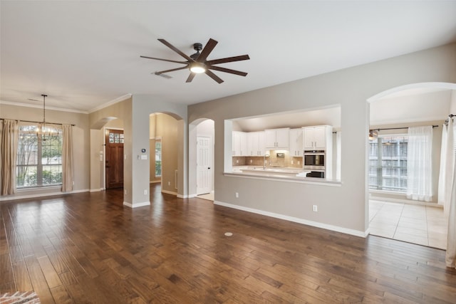 unfurnished living room featuring ceiling fan with notable chandelier, dark hardwood / wood-style floors, and ornamental molding