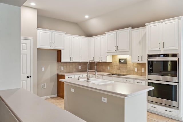 kitchen featuring sink, vaulted ceiling, double oven, light tile patterned flooring, and white cabinetry