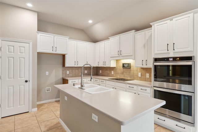 kitchen featuring white cabinetry, stainless steel double oven, sink, and an island with sink