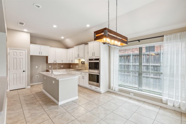 kitchen featuring sink, an island with sink, pendant lighting, vaulted ceiling, and white cabinets