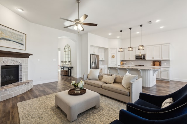 living room featuring ceiling fan, dark wood-type flooring, sink, and a fireplace