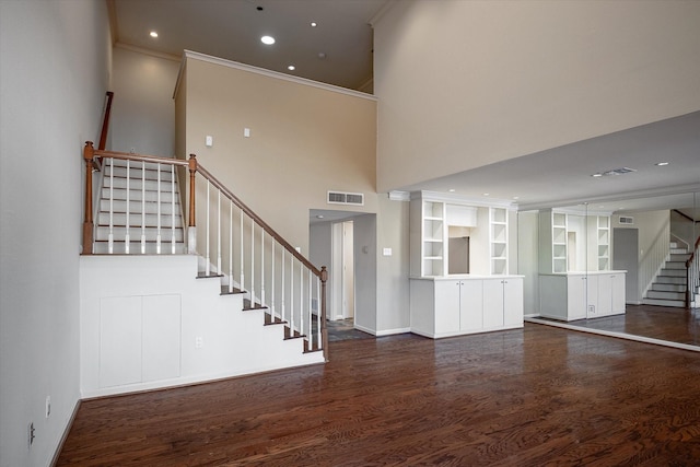 unfurnished living room featuring a high ceiling, ornamental molding, and dark wood-type flooring