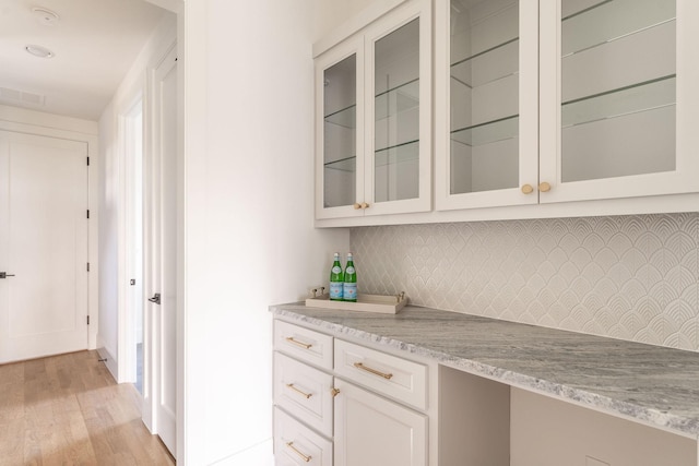 bar featuring light stone counters, tasteful backsplash, built in desk, light hardwood / wood-style floors, and white cabinets