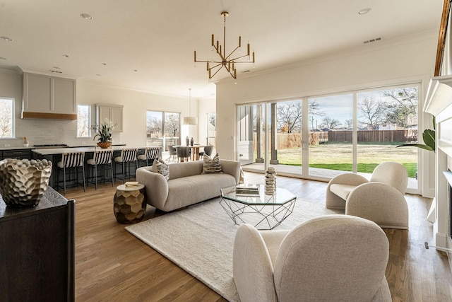 living room with a healthy amount of sunlight, ornamental molding, a chandelier, and light hardwood / wood-style floors