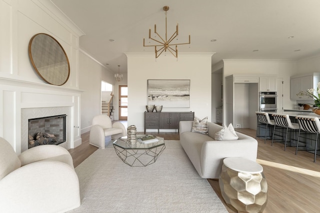 living room with crown molding, a high end fireplace, an inviting chandelier, and light wood-type flooring