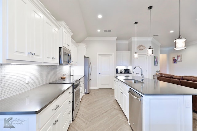 kitchen with appliances with stainless steel finishes, decorative light fixtures, white cabinetry, sink, and a center island with sink