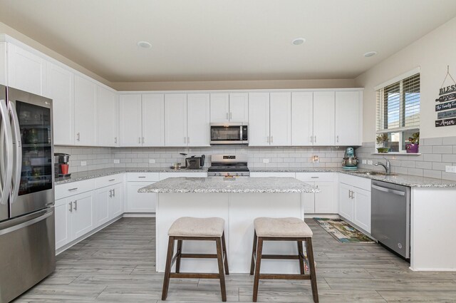 kitchen with white cabinets, light stone countertops, a kitchen island, and appliances with stainless steel finishes