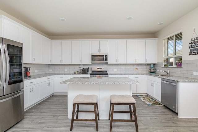 kitchen with white cabinetry, light stone counters, stainless steel appliances, and a center island