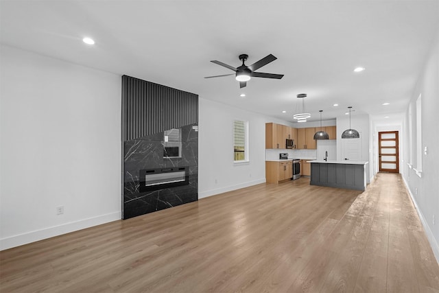 unfurnished living room with light wood-type flooring, ceiling fan, and tile walls