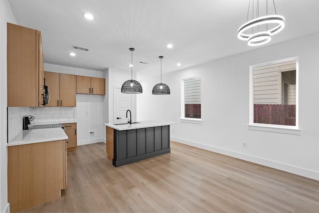 kitchen featuring decorative light fixtures, stove, an island with sink, and light hardwood / wood-style flooring