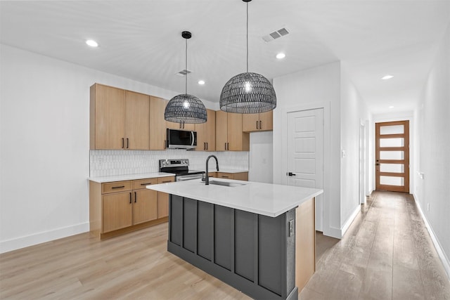 kitchen featuring appliances with stainless steel finishes, sink, a center island with sink, light hardwood / wood-style floors, and hanging light fixtures