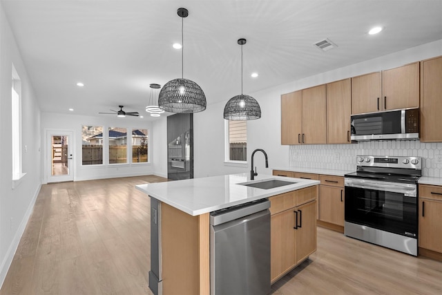 kitchen with sink, stainless steel appliances, light hardwood / wood-style flooring, pendant lighting, and a kitchen island with sink