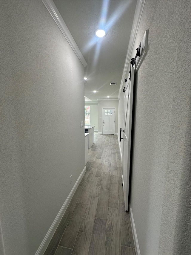 hall featuring a barn door, crown molding, and hardwood / wood-style flooring