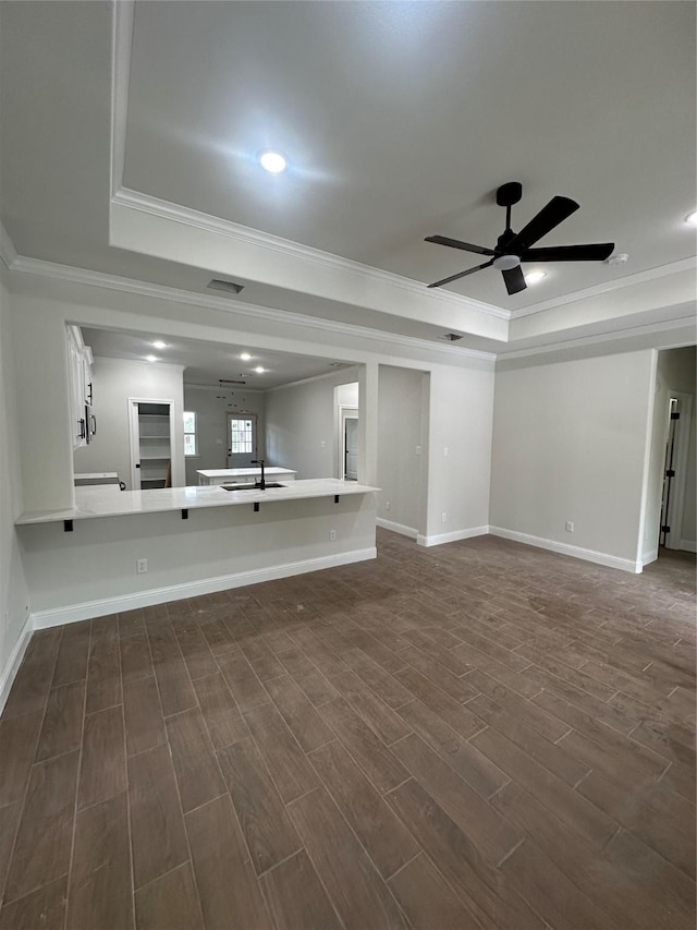 unfurnished living room with a tray ceiling, ceiling fan, dark hardwood / wood-style flooring, and ornamental molding