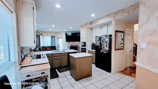 kitchen with black appliances, sink, light wood-type flooring, a kitchen island, and kitchen peninsula