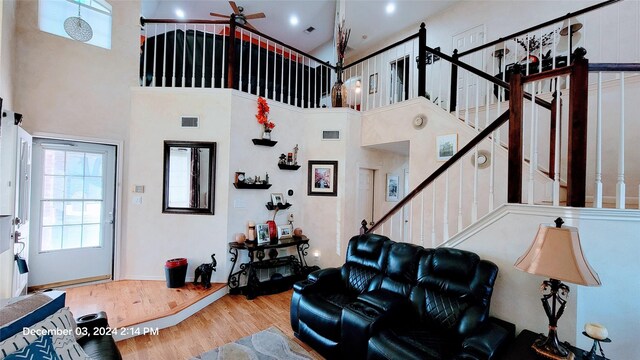 living room featuring wood-type flooring, a towering ceiling, and ceiling fan