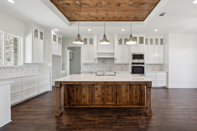 kitchen featuring pendant lighting, dark wood-type flooring, a center island with sink, a raised ceiling, and stainless steel appliances