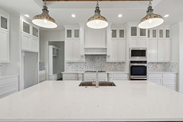 kitchen featuring stainless steel microwave, sink, pendant lighting, a kitchen island with sink, and white cabinets