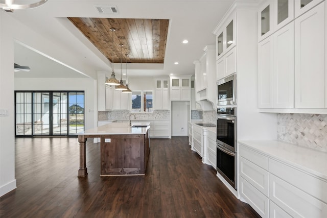 kitchen featuring tasteful backsplash, dark wood-type flooring, white cabinetry, stainless steel microwave, and an island with sink