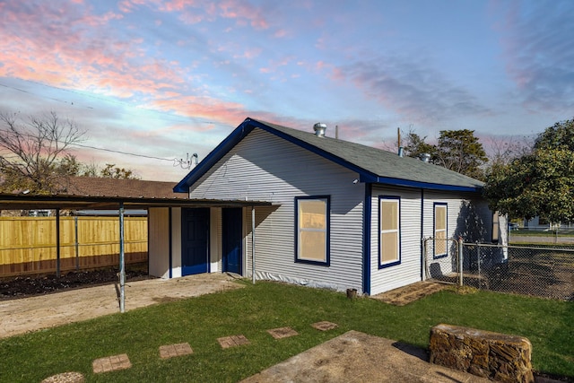 back house at dusk featuring an outbuilding and a lawn