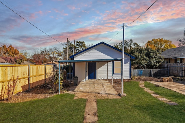 back house at dusk featuring a lawn and a patio