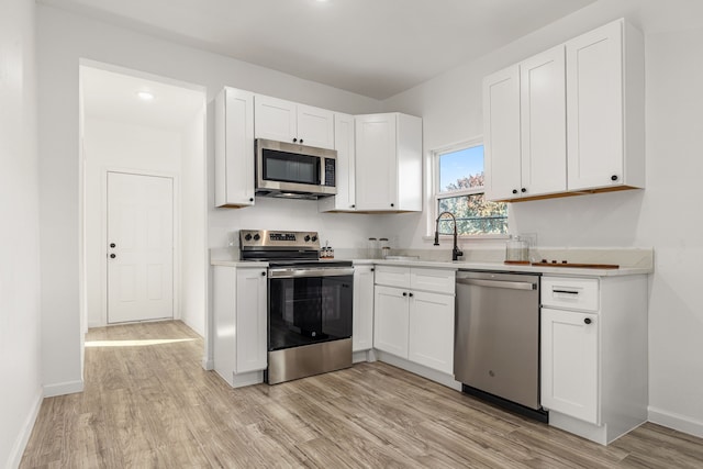 kitchen with appliances with stainless steel finishes, light hardwood / wood-style floors, white cabinetry, and sink