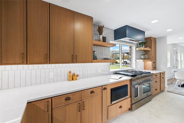 kitchen featuring light stone countertops, tasteful backsplash, range with two ovens, and exhaust hood