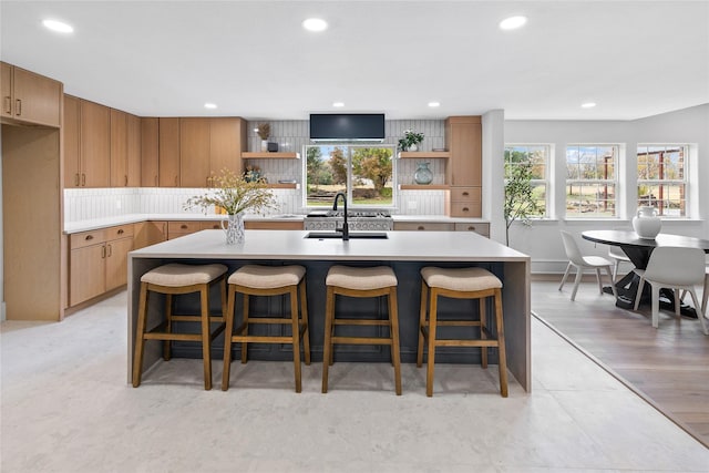 kitchen with a center island with sink, backsplash, light wood-type flooring, and sink