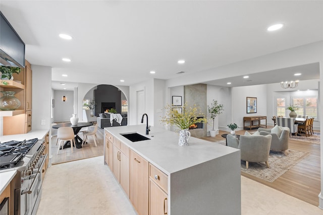 kitchen featuring light brown cabinetry, a large fireplace, a center island with sink, and sink